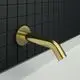 Wandauslauf von Ideal Standard in gebürstetem Gold, montiert an einer Wand mit schwarzen Fliesen. Der Auslauf hat eine fließende, gebogene Form und ist allseitig sichtbar.